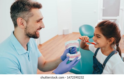 Dentist Teaching Little Mixed Race Girl Brushing Teeth Using Human Teeth Model At Dental Clinic