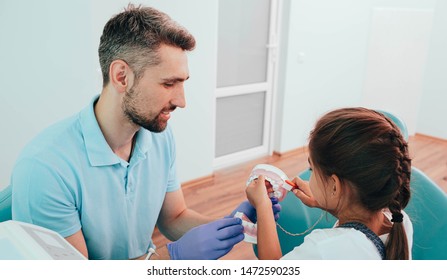 Dentist Teaching Little Mixed Race Girl Brushing Teeth Using Human Teeth Model At Dental Clinic