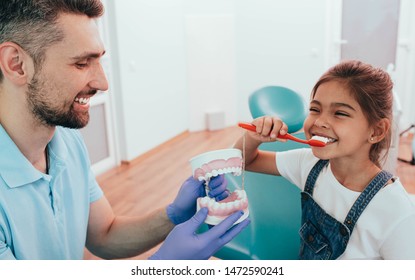 Dentist Teaching Little Mixed Race Girl Brushing Teeth Using Human Teeth Model At Dental Clinic