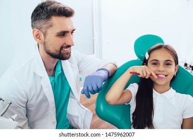 Dentist Teaching Little Mixed Race Girl Brushing Teeth Using Human Teeth Model At Dental Clinic