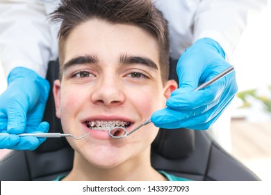 Dentist With Tools In The Young Man's Mouth With Orthodontics