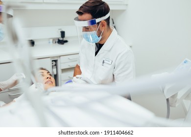 Dentist treating a female patient at dental clinic. Male doctor wearing  mask and face shield discussing treatment with patient at dental clinic. - Shutterstock ID 1911404662
