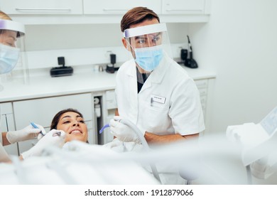 Dentist Treating A Female Patient At Dental Clinic. Male Doctor Wearing  Mask And Face Shield During Dental Treatment Of A Woman.