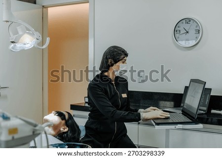 Dentist typing on the computer while preparing for a dental appointment in a modern, bright clinic.