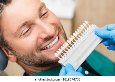 Dentist Uses A Palette Tooth Color Sample To Determine Shade Of Patient's Male Teeth. Stomatologist Use Color Of Teeth To Make Veneers, Crowns, And Dentures