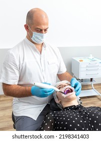 Dentist Using Dental Curing UV Lamp On Teeth Of Patient