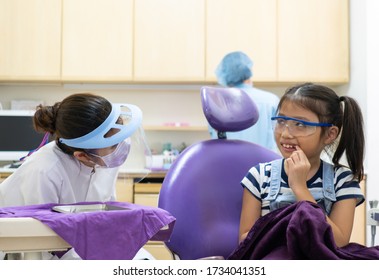 Dentist Using Dental Tools To Clean Teeth Of Asian Child And Treat Tooth Decay In The Clinic With Asisstance Standing Behind The Patient. Dentistry And Healthcare Concept