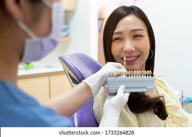 Dentist Using Tooth Color Chart To Compare With Teeth Of Asian Woman Patient Preparing For Laser Tooth Whitening In Dental Clinic. Dentistry And Healthcare Concept