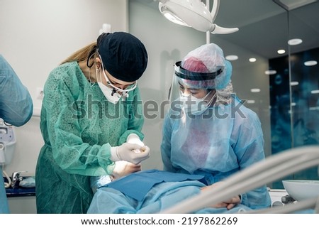 Dentist wearing face mask and dental magnifying glasses doing treatment to unrecognized patient.