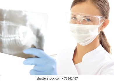 Dentist Wearing A Surgical Mask And Goggles, Looks At The Camera As She Holds Up An X-ray Image. Horizontal Shot.