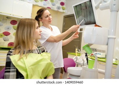 Dentist Woman Doing Review Of Young Woman, Female Patient Sitting In Armchair At Dental Clinic. Dentist Female Explaining X-Ray To Patient. Dentistry, Medicine And Health Care Concept