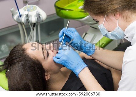 Dentist at work examining woman's teeth in dental clinic. Patient has piercing or noseRings in the nose 