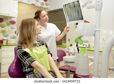 Dentistry, Medicine And Health Care Concept. Dentist Woman Doing Review Of Young Woman, Female Patient Sitting In Armchair At Dental Clinic. Dentist Female Explaining X-Ray To Patient. 