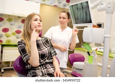 Dentistry, Medicine And Health Care Concept - Young Beautiful Woman 25 Years Old On Review Of Dentist, Sitting In Dental Armchair. Dentist Female Explaining X-Ray To Young Cute Girl.