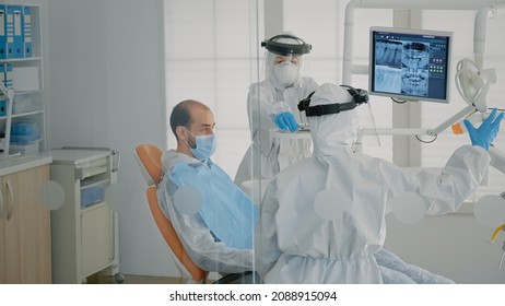 Dentistry Staff Wearing Ppe Suits Doing Teethcare Consultation On Patient, Using Dental Equipment In Stomatology Cabinet. Dentist And Specialist Working On Oral Examination At Clinic.