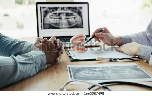 Dentists are discussing dental\
problems at report x-ray image on laptop screen to\
patients.
