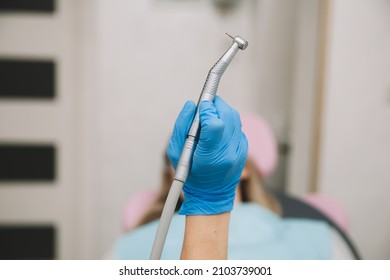 Dentist's hand holding a dental drill with a turbine. patient in the background with open mouth.