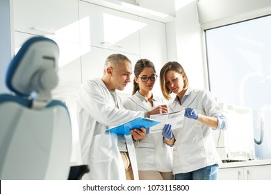 Dentists Team In Dental Office Examining List Of Patients.
