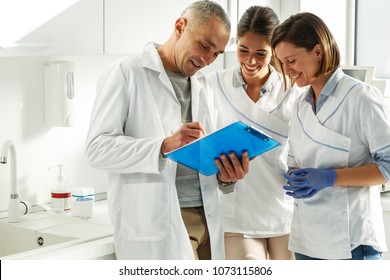 Dentists Team In Dental Office Examining List Of Patients.
