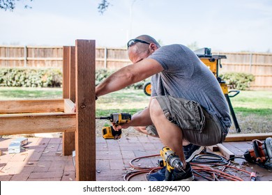 Denton, TX / USA - March 12, 2020: Side View Of Man As He Drills With A Cordless Electric Power Screwdriver To Place Screws Into A Wooden Post For A DIY Project Constructing A Raised Container Garden.