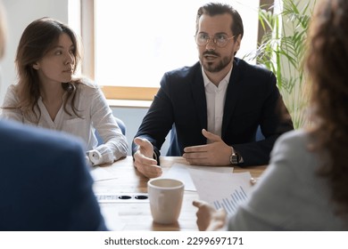 Department brainstorming in office board room, staff led by male CEO discussing new project, sharing ideas thoughts and sales statistics, provide information to shareholders engaged in formal meeting