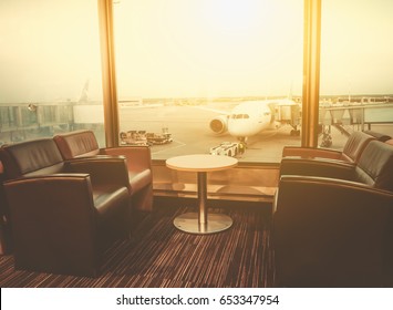 Departure lounge at the airport with seating and table with aircraft preparing for flight in the background - Shutterstock ID 653347954