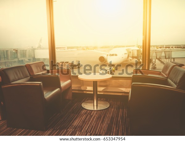 Departure lounge\
at the airport with seating and table with aircraft preparing for\
flight in the\
background