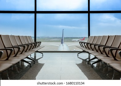 Départ du salon à l'aéroport avec des places en rangée, l'avion et le ciel bleu derrière les fenêtres.