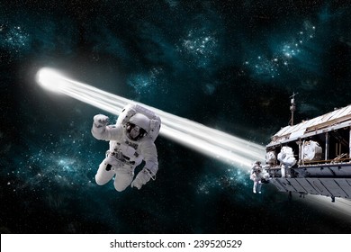 A depiction of an astronaut floating in outer space while his fellow astronauts work on a space station.  A comet passes dangerously close to their location. Elements of this Image Furnished by NASA. - Powered by Shutterstock