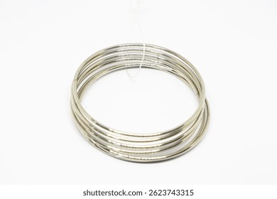 Depicts a stack of thin, shiny silver metal bangles arranged concentrically on a clean white surface. A fine, transparent string is subtly visible.