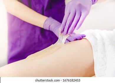 Depilating legs young woman with liquid sugar pasta in spa salon.