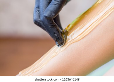 depilation and beauty concept - procedure of hair removing on leg beautiful woman with sugar paste or wax honey and black gloves hand