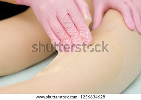 depilation and beauty concept - procedure of hair removing on leg beautiful woman with sugar paste or wax honey and pink gloves hand