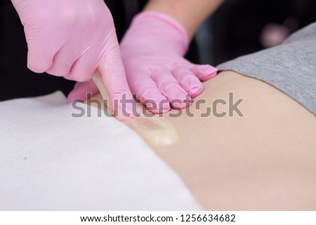 depilation and beauty concept - procedure of hair removing on leg beautiful woman with sugar paste or wax honey and pink gloves hand