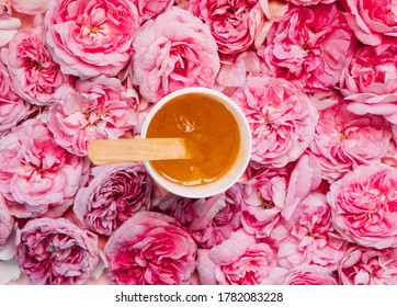 depilation and beauty concept - sugar paste or wax honey for hair removing flows down from wooden waxing spatula sticks on flower background. copyspase.