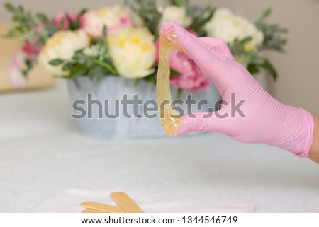 depilation and beauty concept - sugar paste or wax honey for hair removing with pink gloves hands of cosmetologist in spa salon