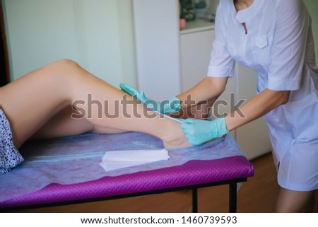 The Depilation Wizard applies wax to a woman’s leg, applying a strip of material to hot wax to remove hair.