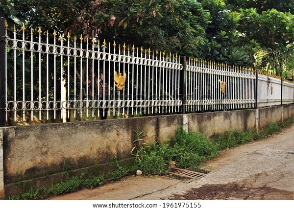 Depok, West Java, Indonesia - April 2021 : White\
fence with various ornaments is a dividing area of ​​private\
property from the main\
road