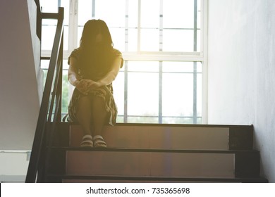 depress and hopeless woman sitting on ladder in house with arm around knee and lower head, abuse concept