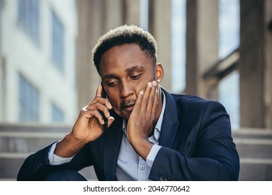 Depressed African American Businessman Telling Sad News Talking On Cell Phone Sitting On Office Stairs In Business Suit