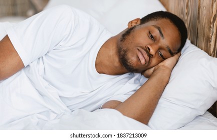 Depressed African American Guy Lying Awake In Bed Having Insomnia At Night In Bedroom At Home. Male Apathy And Depression Problem, Sleeplessness And Stress Concept.