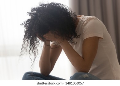 Depressed african American young woman sit at home feel desperate down suffering from relationships problems breakup, upset black girl crying having life troubles, miscarriage or abortion concept