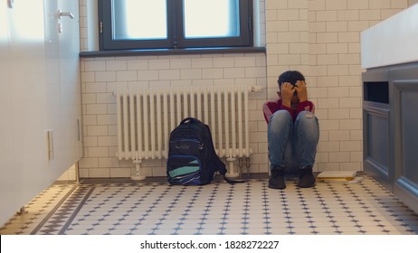 Depressed african child abandoned in lavatory and leaning against wall. Young afro boy sitting alone with sad feeling at school. Bullying, discrimination and racism concept - Shutterstock ID 1828272227