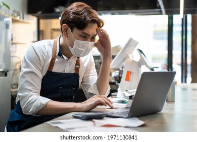 Depressed Asian Cafe Owner Wear Protective Mask During Covid19 Pandemic Feel Worried About Financial Problem In Coffee Shop. Stressed Barista Look Frustrated To Bills And Payment Of His Small Business