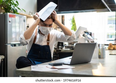 Depressed Asian Cafe Owner Wear Protective Mask During Covid19 Pandemic Feel Worried About Financial Problem In Coffee Shop. Stressed Barista Look Frustrated To Bills And Payment Of His Small Business