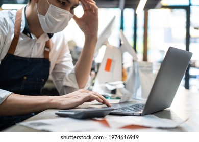 Depressed Asian Cafe Owner Wear Protective Mask During Covid19 Pandemic Feel Worried About Financial Problem In Coffee Shop. Stressed Barista Look Frustrated To Bills And Payment Of His Small Business