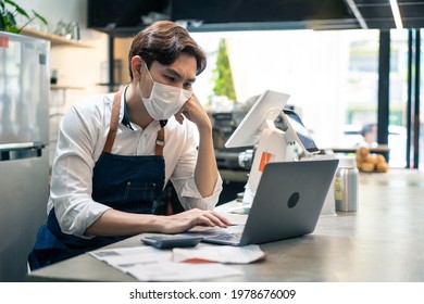 Depressed Asian Cafe Owner Wear Protective Mask During Covid19 Pandemic Feel Worried About Financial Problem In Coffee Shop. Stressed Barista Look Frustrated To Bills And Payment Of His Small Business