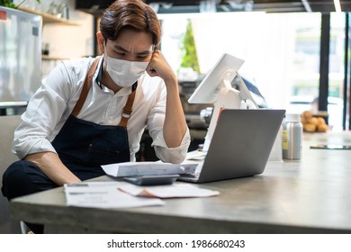 Depressed Asian Cafe Owner Wear Protective Mask During Covid19 Pandemic Feel Worried About Financial Problem In Coffee Shop. Stressed Barista Look Frustrated To Bills And Payment Of His Small Business