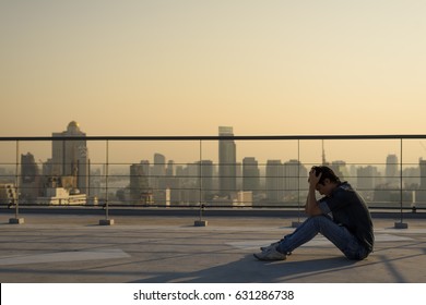 Depressed asian man is hands on head and sitting on the rooftop of the building on the bangkok cityscape at the sunset time look like silhouette, dramatic concept, Have copy space - Powered by Shutterstock