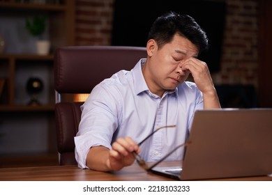 Depressed Asian Man Is Sitting In The Office. Massages The Bridge Of The Nose From Eye Fatigue. Poor Vision After The Screen. Stress, Fatigue, Burnout, Apathy.